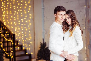 Beyaz kazak Noel ışıkları ile odada ayakta poz sarılma aşık genç Çift