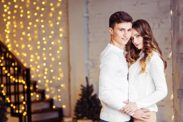 Beyaz kazak Noel ışıkları ile odada ayakta poz sarılma aşık genç Çift