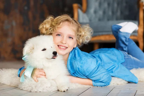 金髪少女の白いふわふわの子犬と床に横たわってポーズ — ストック写真