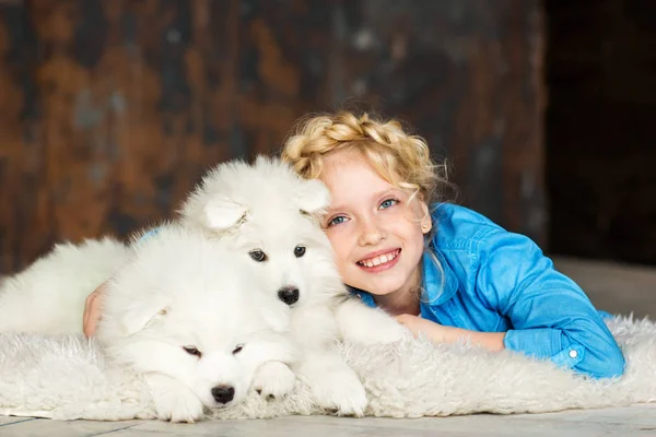 つの白いふわふわの子犬と床に横たわってポーズ金髪少女 — ストック写真