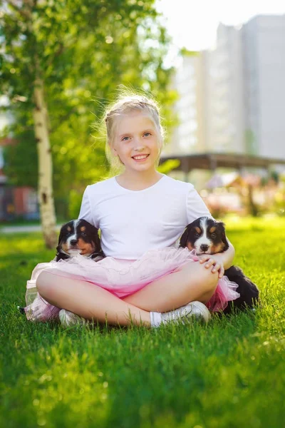 緑の草の上に座ってかわいい子犬を抱いて金髪少女 — ストック写真