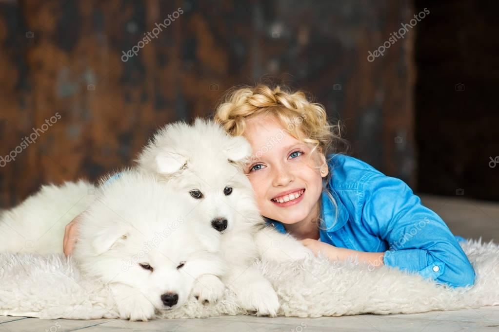 little blonde girl posing lying on floor with two white fluffy puppies