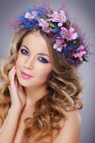 灰色の背景の上ポーズ ピンクとブルーの花の花輪を身に着けている若い美しい女性の肖像画 — ストック写真