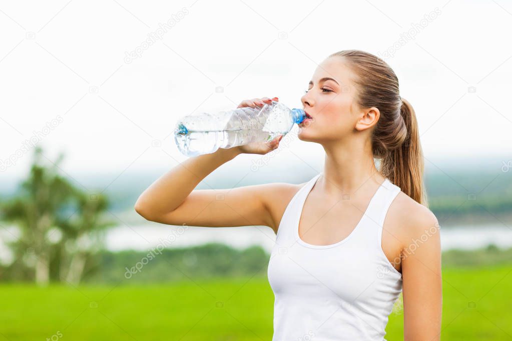 portrait of young sporty woman drinking water after workout outdoor