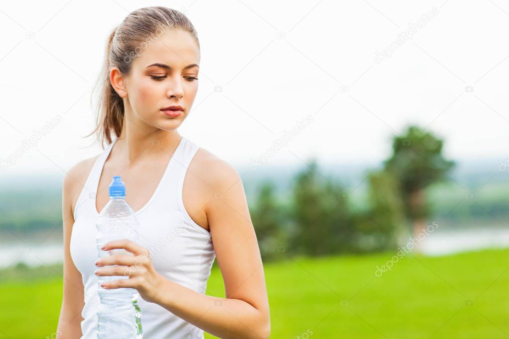 portrait of young sporty woman holding bottle of water after workout outdoor