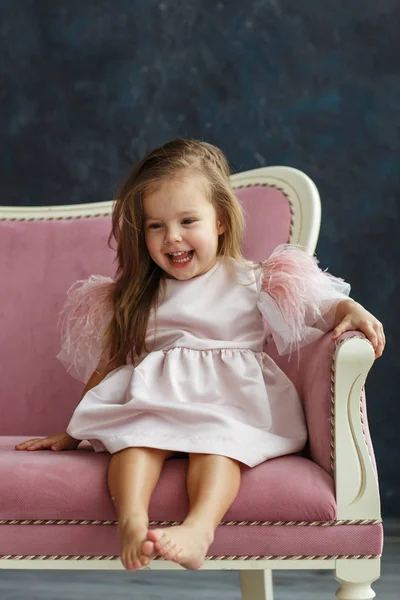 Cute little model in pink dress sitting on the sofa