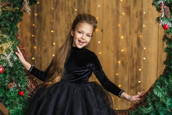 attractive little girl in black dress sits in a Christmas wreath