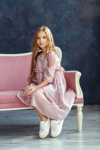 Cute little model in pink dress sitting on the sofa