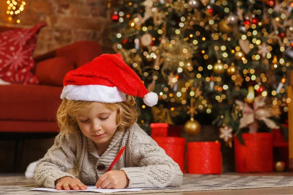 小さな巻き少年はクリスマスツリーの近くにサンタに手紙を書く — ストック写真