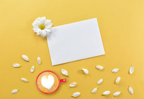 Good morning. Cup of coffee with a heart and a card with copy space for text, on a yellow background. Cup of coffee with petals of chamomile flowers on a yellow background. View from above.Flat lay.