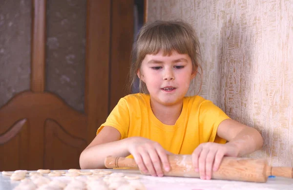 Little girl rolls the dough and flour. Little girl sculpts from the dough. The girl kneads the dough.