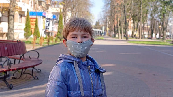 A little girl walks in the park in a mask. A little girl walks through an empty city and covers her face with a mask from a coronavirus. Coronavirus epidemic.