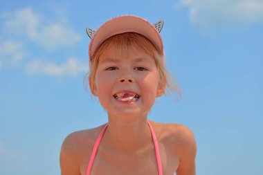 Kumsaldaki küçük kız şeker yiyor. Denizde küçük bir kızın yaz tatili. Dişinde şeker tutan küçük bir kız.