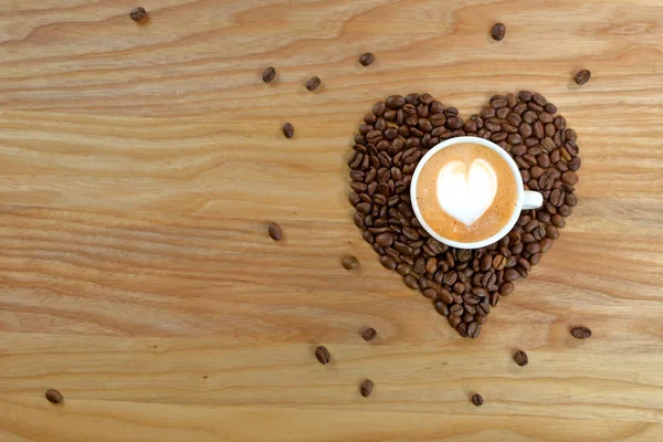 Heart made from coffee beans, with a cup on a wooden background. A cup of coffee on a wooden table.