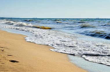 Sea waves wash the beach against a blue sky. clipart