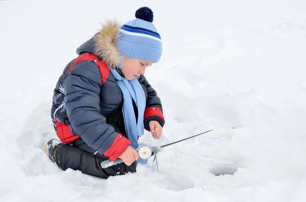Little boy fishing on the frozen river in winter Stock Photo