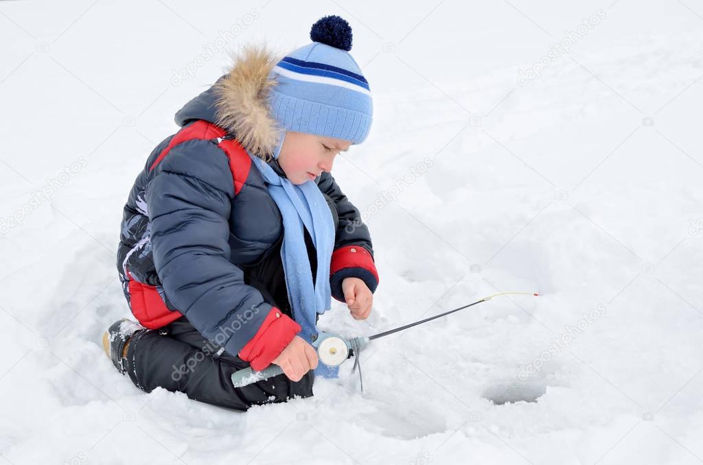 Little boy fishing on the frozen river in winter