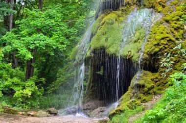 Bir mağara arasında yeşil bir bahçe şelale