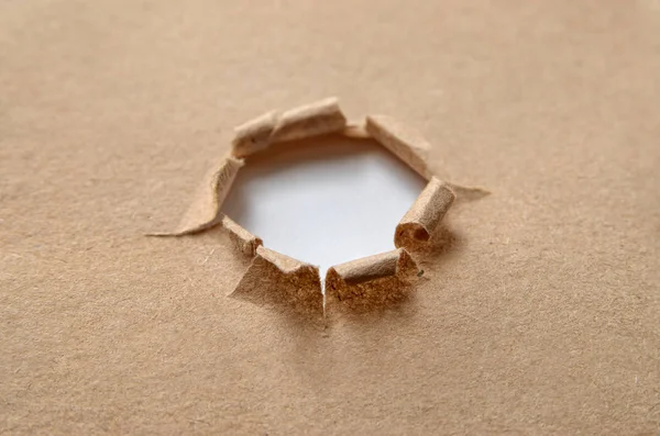 在粗糙的褐色纸上的一个破圆孔 — 图库照片