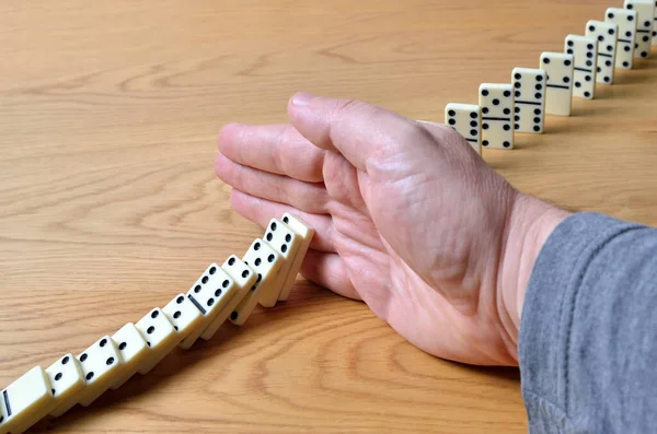 Domino effect, chain reaction is stopped by a human hand.