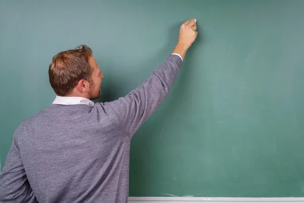 Male teacher writing on a blank chalkboard — Stock Photo, Image