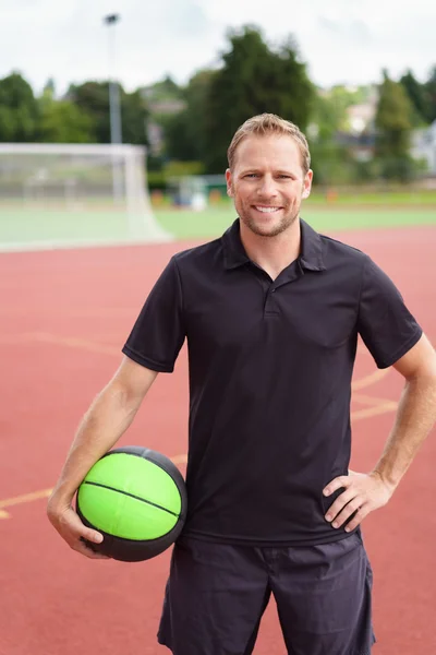 Atletische man die op een baan met een bal — Stockfoto