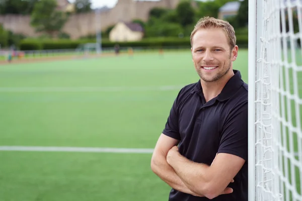 Relajado entrenador de fútbol feliz apoyándose en el gol — Foto de Stock