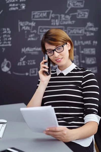Lehrerin telefoniert mit Handy und überprüft Klassenarbeiten — Stockfoto