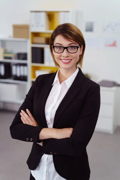 Vrouw in jas met gevouwen armen in kantoor — Stockfoto