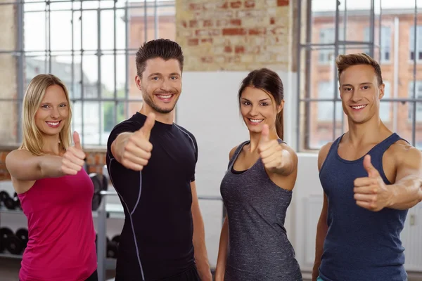 Quatre jeunes adultes attirants à la salle de gym avec les pouces levés — Photo