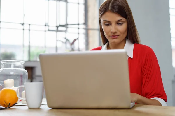 Jonge vrouw die werkt op een laptop in de keuken — Stockfoto