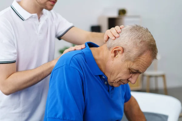 Fisioterapeuta masajeando cuello de paciente mayor — Foto de Stock