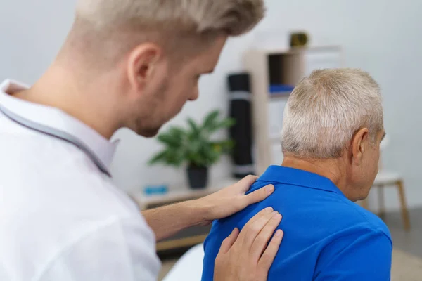 Fisioterapeuta examinando la espalda del paciente anciano — Foto de Stock
