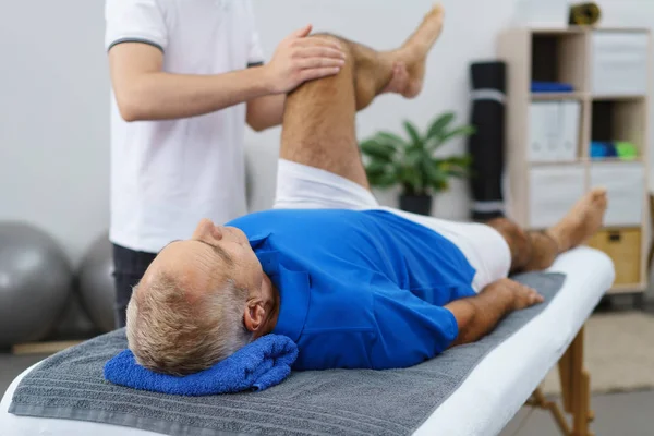 Physiotherapeut manipuliert Bein eines älteren Mannes — Stockfoto