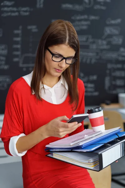 Woman carrying office binders checking her phone — Stock Photo, Image
