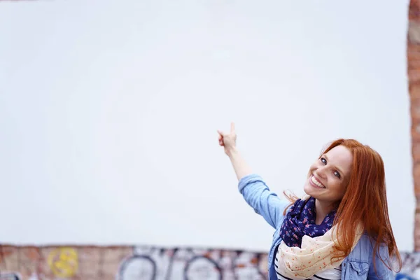 Donna sorridente che punta alla zona bianca sul muro — Foto Stock