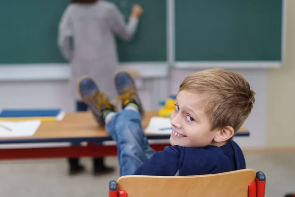 Улыбающийся мальчик с поднятыми ногами в классе — стоковое фото