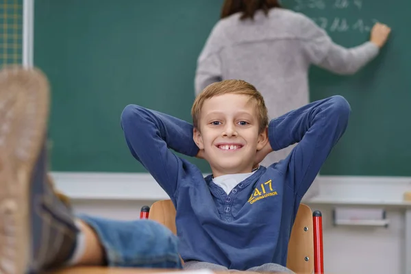Roztomilý mladý chlapec s nohama nahoru ve třídě — Stock fotografie