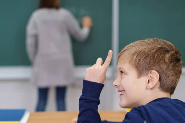 Rire jeune garçon levant le doigt en classe — Photo