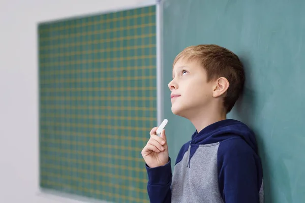 Thoughtful young boy holding chalk in class — Stock Photo, Image