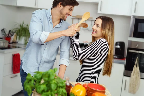 笑对年轻夫妇模拟战斗在厨房里 — 图库照片