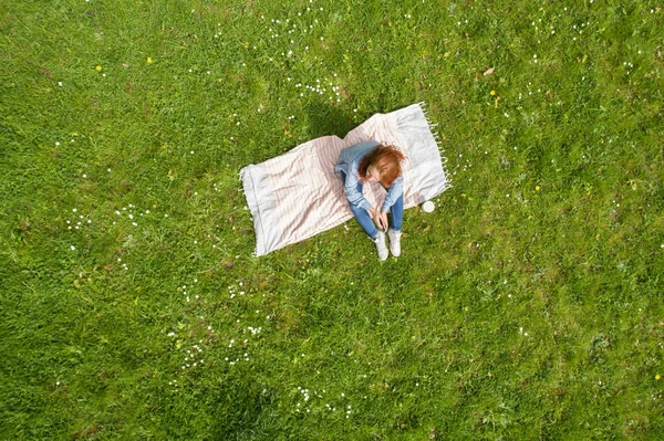 Eenzame jonge vrouw ontspannen op een tapijt op gras — Stockfoto
