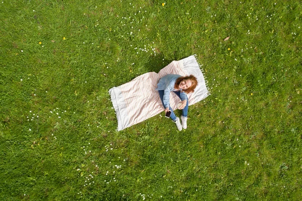 Jonge vrouw rustend op een deken op gras opzoeken — Stockfoto
