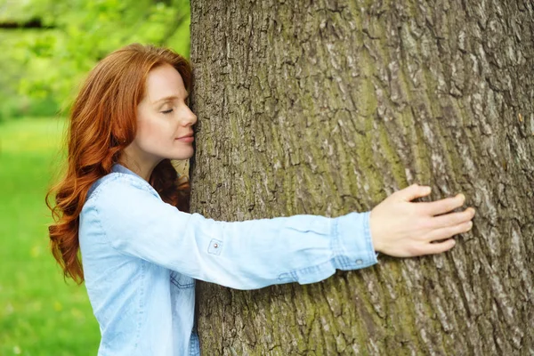 Νεαρή γυναίκα αγκαλιάζει ένα κορμό δέντρου σε ένα πάρκο — Φωτογραφία Αρχείου
