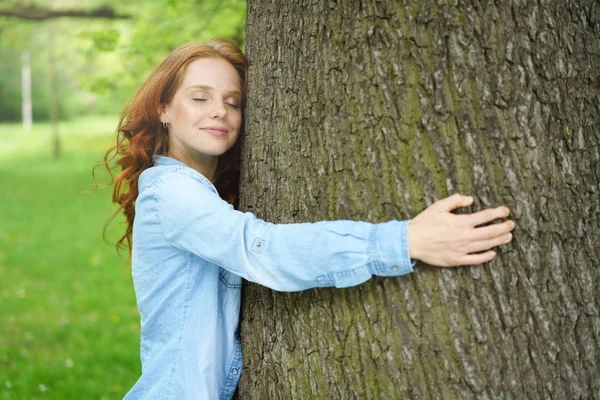 Satisfait jeune femme étreignant un grand arbre — Photo