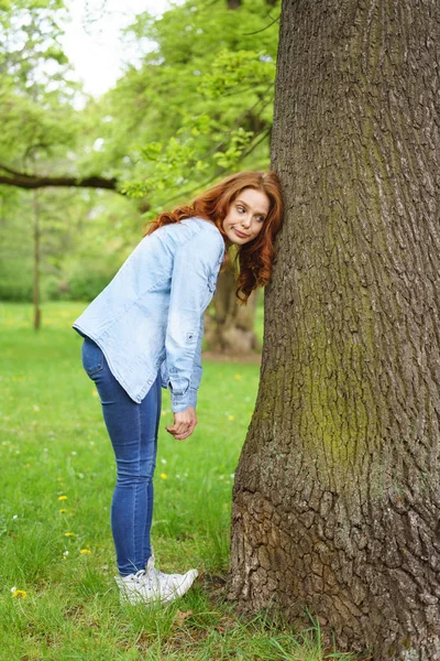 Woman with a wry expression leaning on a tree — Stock Photo, Image