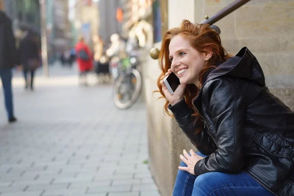 Donna siede in una strada della città a parlare sul suo cellulare — Foto Stock