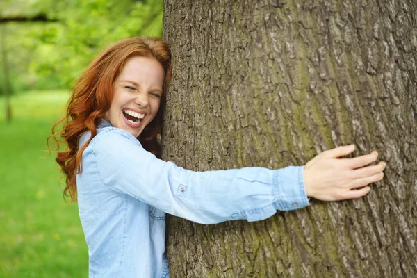 Rindo jovem mulher abraçando uma grande árvore — Fotografia de Stock