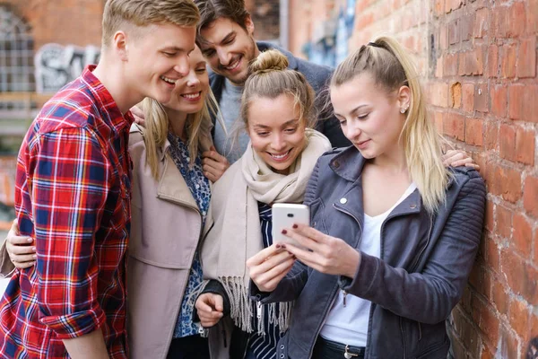Groep jonge vrienden kijken naar mobiele telefoon — Stockfoto