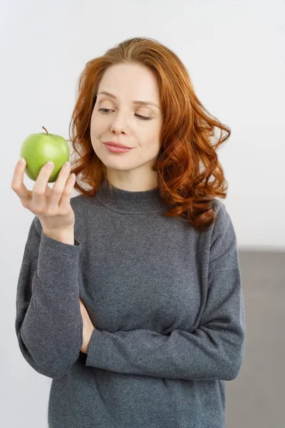 Jovem pensativa olhando para uma maçã verde fresca — Fotografia de Stock